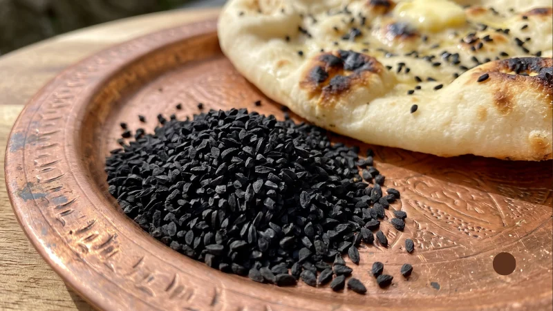 Seeds in Hindi: Names, Benefits & Best Season 7 Angular black kalonji seeds on a copper plate next to a fresh naan bread, showing nigella seeds in Hindi.